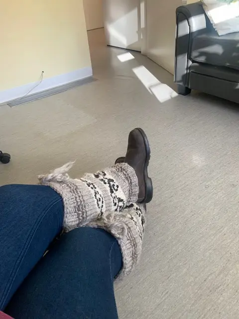 An individual in a warm sweater and trendy boots poses, highlighting a blend of comfort and style in their outfit.